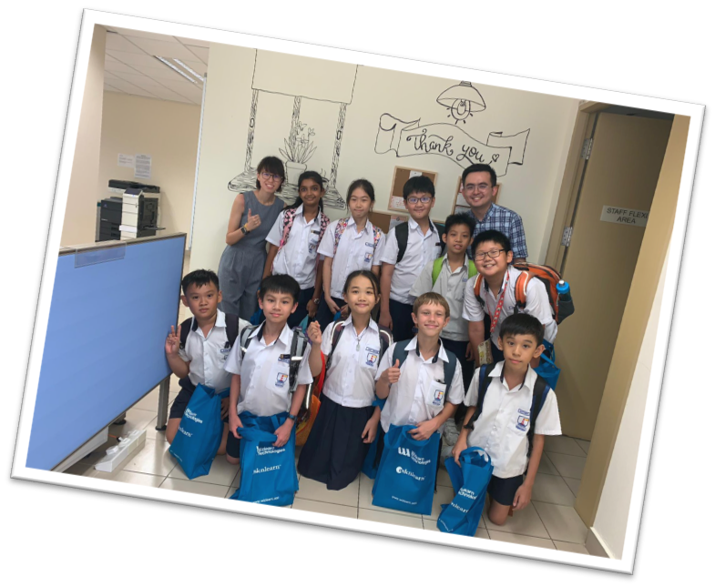 Group of children in school uniforms and two adults posing indoors near a Thank You wall drawing.